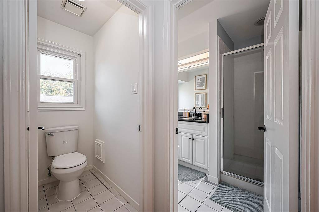 This photo shows a bright bathroom with a separate toilet area, a glass-enclosed shower, and a vanity with a black countertop. The space is well-lit and has a clean, modern design.