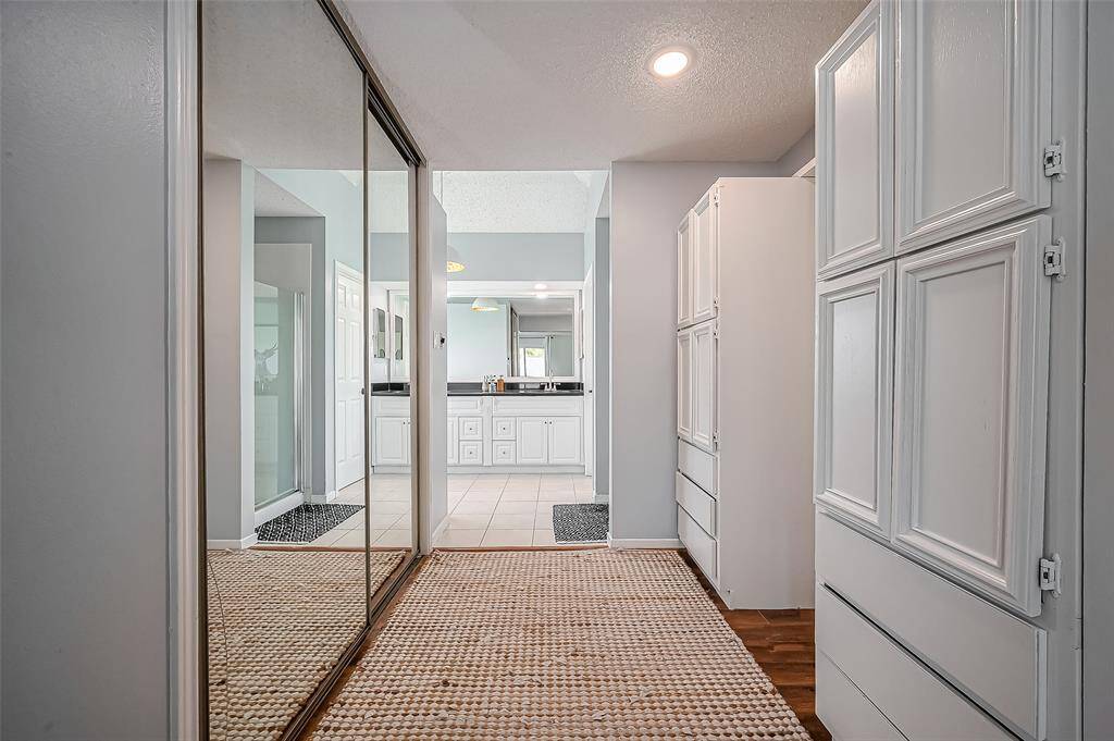 The photo showcases a bright hallway with mirrored sliding closet doors on one side and built-in cabinets on the other. The space leads to a well-lit bathroom featuring dual sinks and ample storage, creating a modern and functional area.