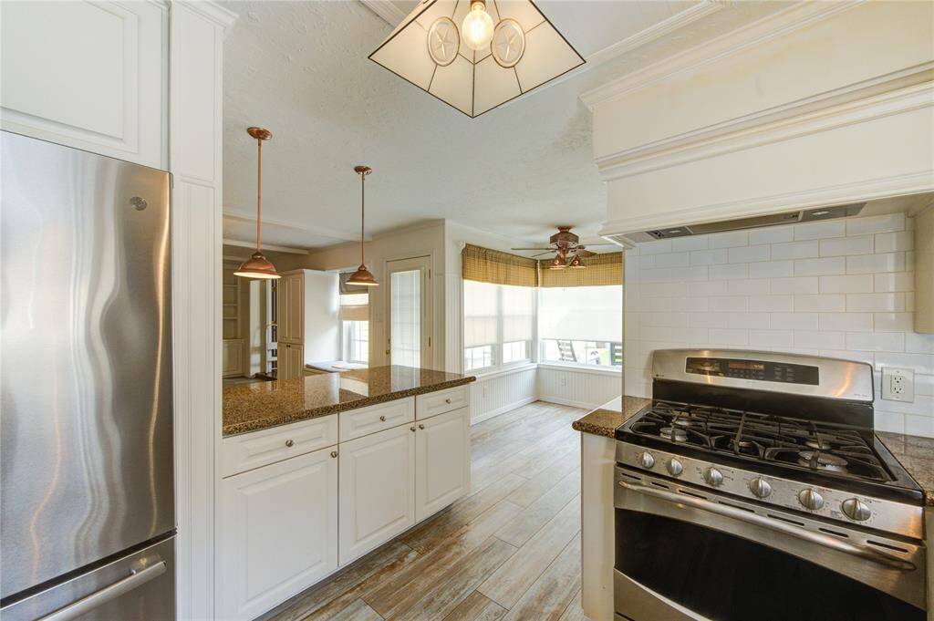 kitchen with granite countertops, stainless steel gas range, and a sunny breakfast nook framed by wraparound windows and warm wood-style flooring. The refrigerator can stay with the home