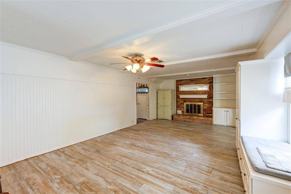 The spacious living area features a cozy brick fireplace with built-in shelving, wide plank wood-look tile flooring, and a charming window seat that invites natural light and relaxation.
