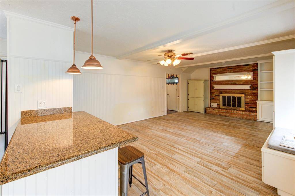 The open-concept layout connects the kitchen’s granite peninsula and bar seating to a spacious living room with cozy fireplace, built-ins, and warm wood-look tile floors throughout.