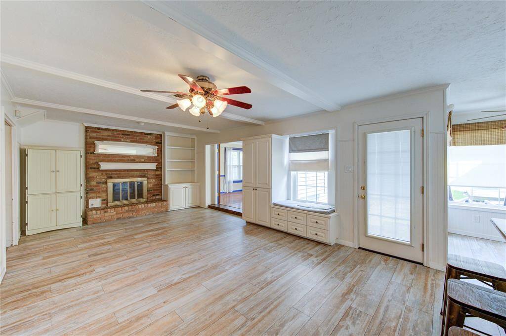 This inviting living space features rich wood-look tile, a classic brick fireplace flanked by built-in shelving, a cozy window seat with storage, and easy access to the backyard and adjacent dining area.