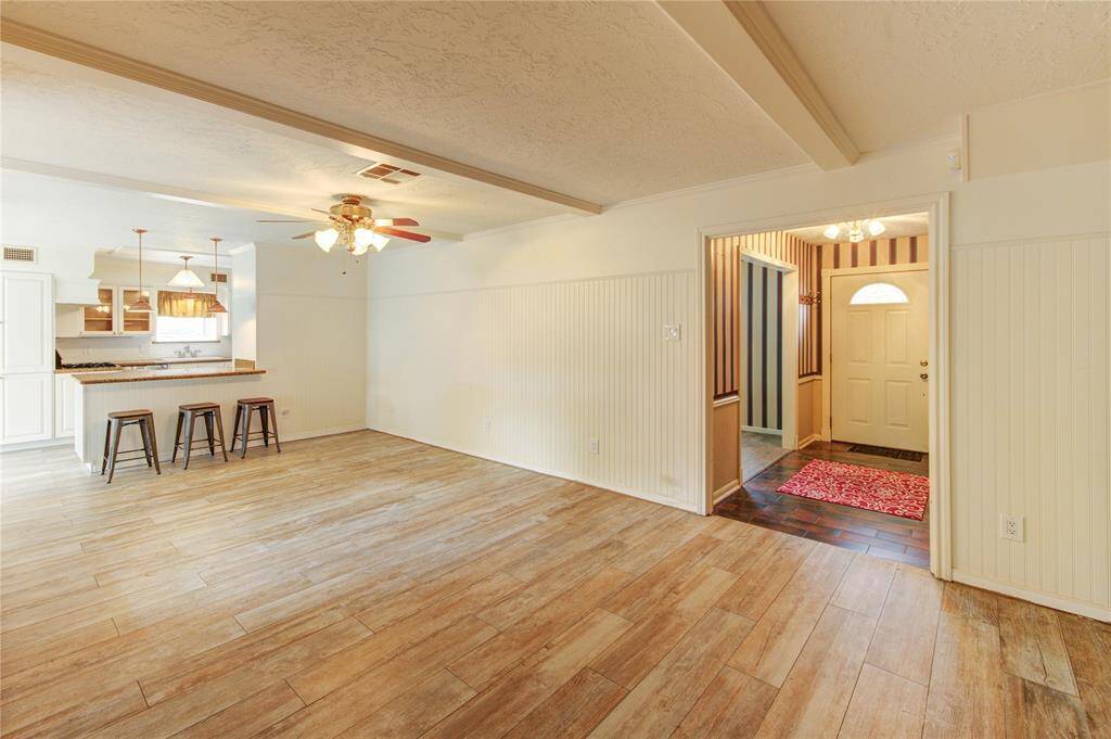 This open living area features classic beadboard wainscoting, a breakfast bar with seating for three, and direct access to the kitchen and front entryway.