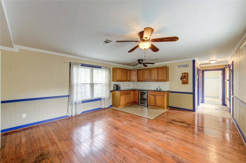 The living room in the mother-in-law suite features a full wall of cabinetry with a sink and beverage fridge, two ceiling fans, and generous natural light from a large window—ideal for comfortable,  or guest use.