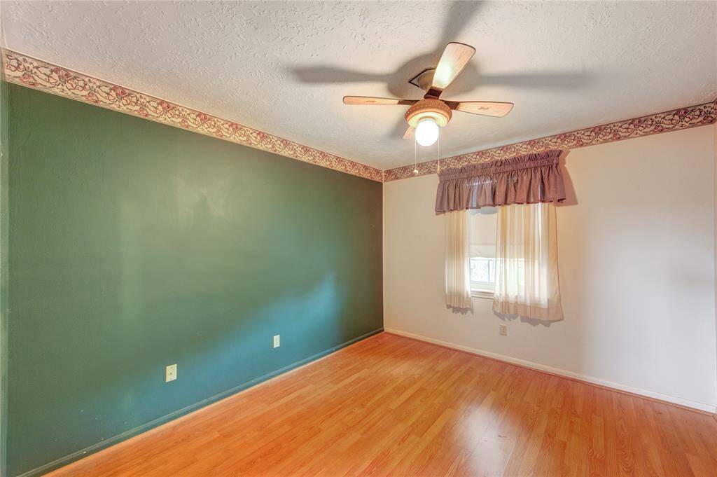 This upstairs secondary bedroom features laminate wood flooring, a ceiling fan, and a large accent wall