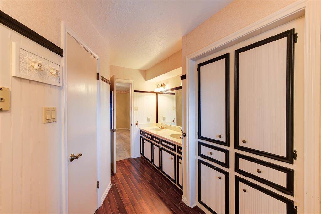 The en suite features dual sinks, beadboard-style cabinetry with bold trim, and abundant built-in storage, all set on wood-look tile for easy maintenance and style.