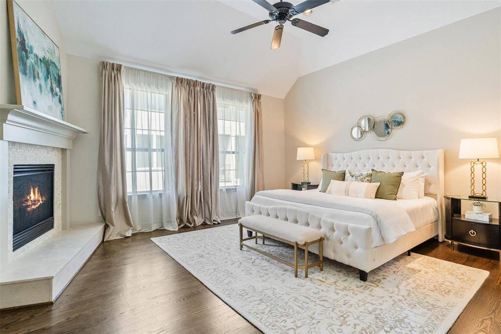 Soft morning light filters through elegant drapes, casting a warm glow across this serene primary retreat. A cozy corner fireplace adds both visual charm and comfort—making the space feel like a true haven at any time of day.