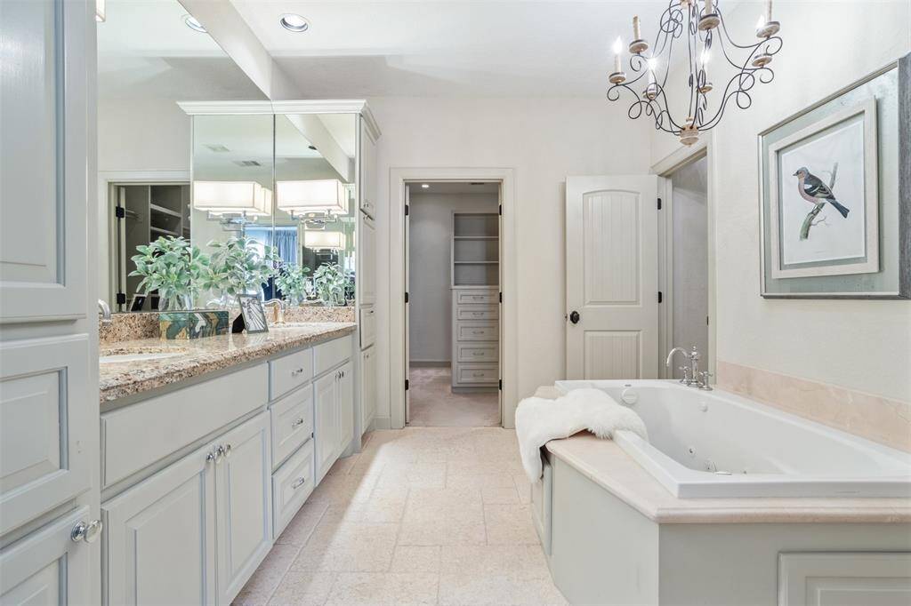 Elegantly appointed with dual vanities, a deep jetted tub, and custom cabinetry, the primary bathroom is your personal retreat. A statement chandelier adds a touch of romance, while the walk-in closet just beyond offers generous, built-in storage to keep everything beautifully organized.