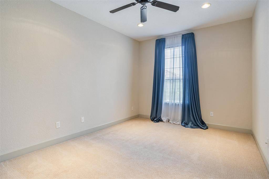 This bright and spacious bedroom features plush carpet, recessed lighting, and a ceiling fan for year-round comfort. The large window with dramatic drapes brings in soft natural light, making the room feel open and inviting.
