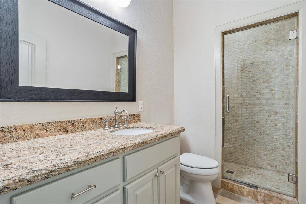 Serving the two secondary bedrooms, this well-appointed bathroom features a granite-topped vanity, sleek chrome fixtures, and a frameless glass shower with stone tile surround—delivering both style and functionality for everyday comfort.