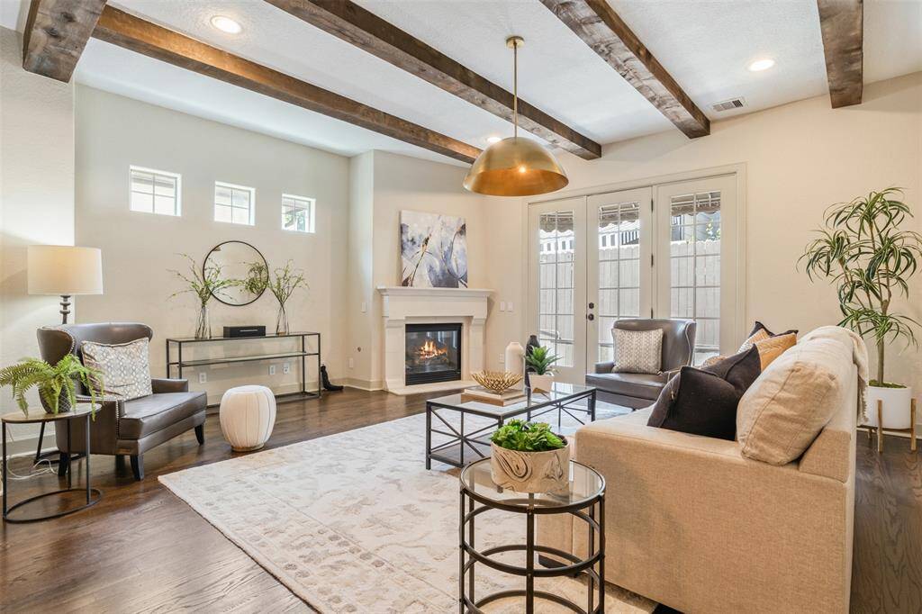 Warmth and elegance define this living room, where exposed beams, a cozy fireplace, and soft natural light set a calming tone. French doors open to the private patio, effortlessly blending indoor comfort with outdoor charm—perfect for slow mornings or evening gatherings under the stars.