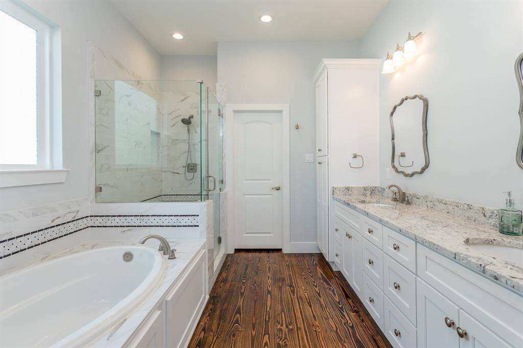 The primary bathroom has double vanities, a soaking tub, oversized shower, linen cabinets, and a tempered glass window. The door pictured leads to the toilet. *Tenant occupied until 05/31/25.*