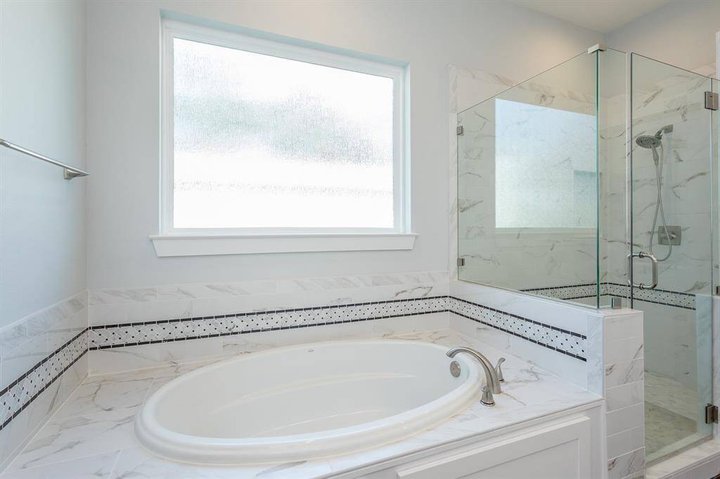 Indulge in the luxurious primary bath featuring an oversized soaking tub, a spacious walk-in shower with marble tile and built-in bench, and a large frosted window that fills the space with soft natural light while maintaining privacy.
