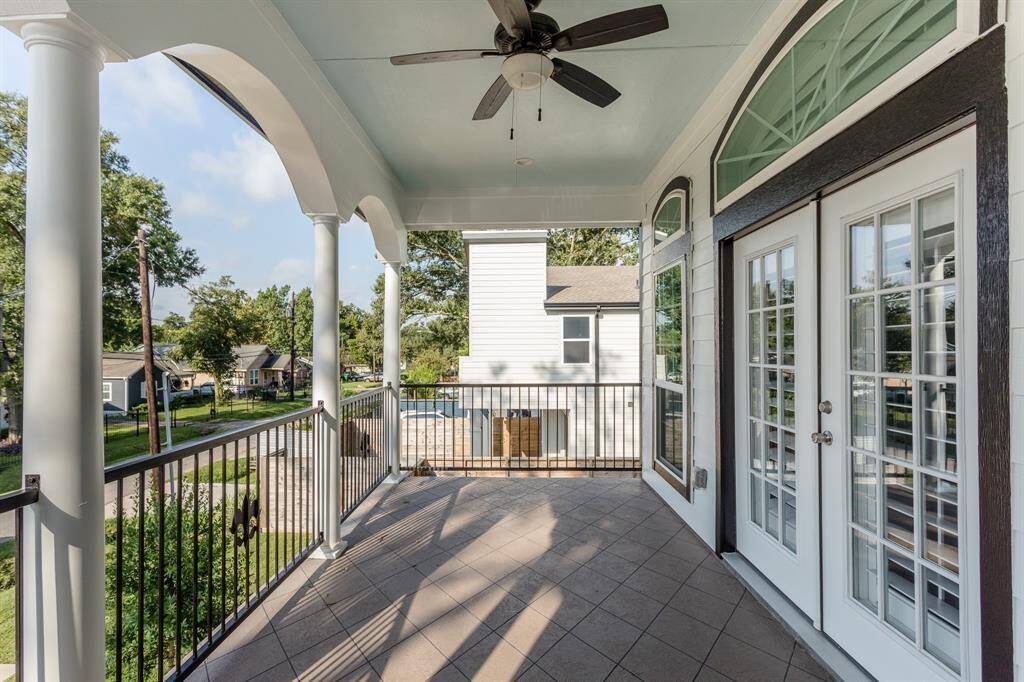 Spacious covered terrace off the primary suite, featuring tile flooring, classic columns, a ceiling fan, and stunning views of the surrounding neighborhood and city skyline.