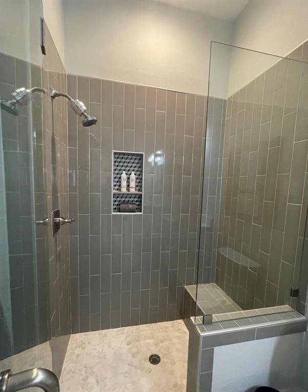Stylish walk-in shower in the downstairs bath features floor-to-ceiling modern gray subway tile, a built-in bench, mosaic tile niche for storage, and pebble-style flooring for a spa-inspired touch.