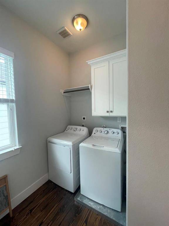 Bright laundry nook includes full-size washer and dryer, overhead cabinet storage, and a hanging rod for convenience, all framed by rich hardwood floors and natural light.