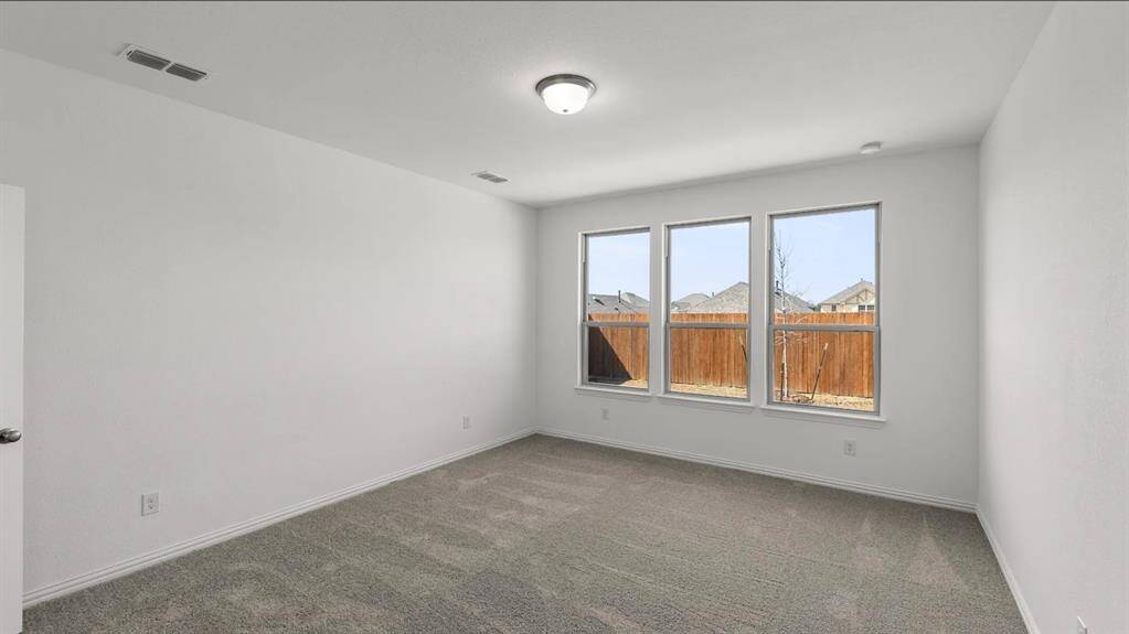 As you enter the primary bedroom, you’re greeted by an abundance of natural light pouring in through large, beautifully framed windows, casting a warm glow on the soft, neutral tones of the walls.
