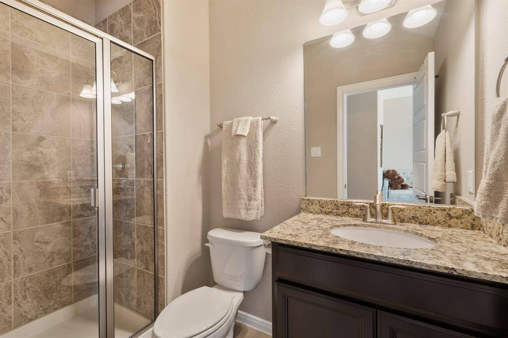 This bathroom features a glass-enclosed shower with textured tile, a granite countertop with an under-mount sink, and warm lighting fixtures.