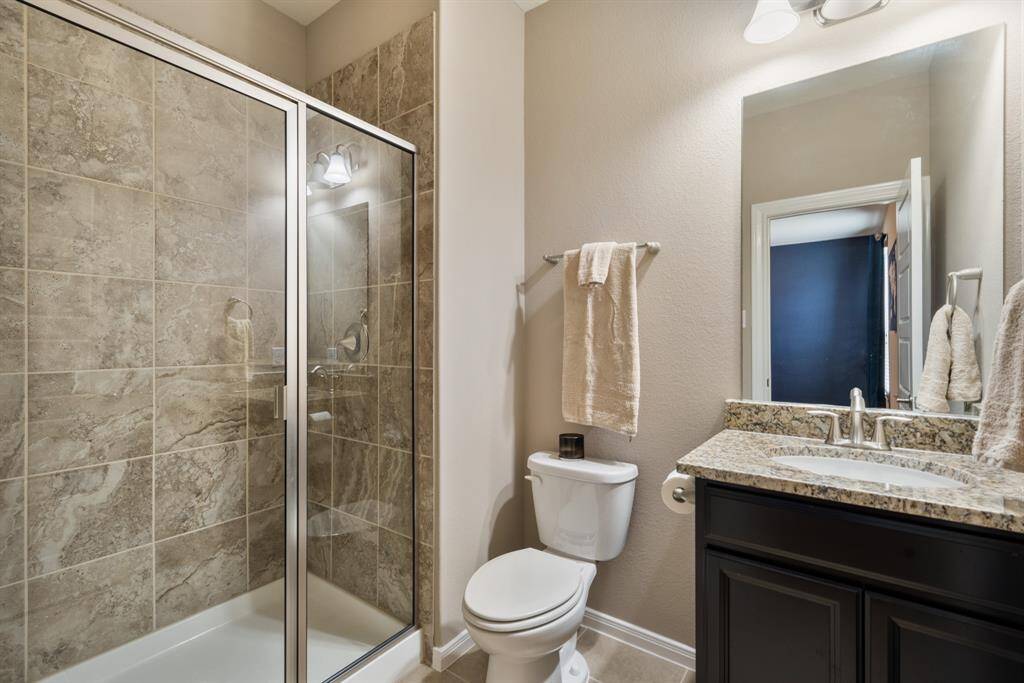 This ensuite bathroom features a sleek glass-enclosed shower with elegant tile work, a granite countertop with a modern sink, and stylish lighting.