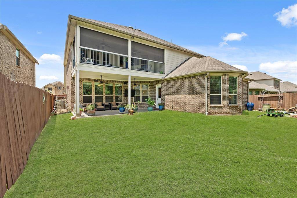 This photo showcases a spacious backyard with a well-maintained lawn, a charming brick exterior, and a retractable screened-in upper balcony. The lower patio is ready for your next bar-b-que gathering!