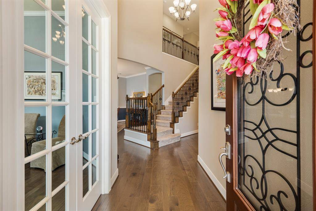 This inviting entryway features engineered flooring leading to a staircase with elegant iron railings. A wooden iron glass door opens into a well-lit space with glass-paneled French doors to the Study, showcasing a cozy seating area.