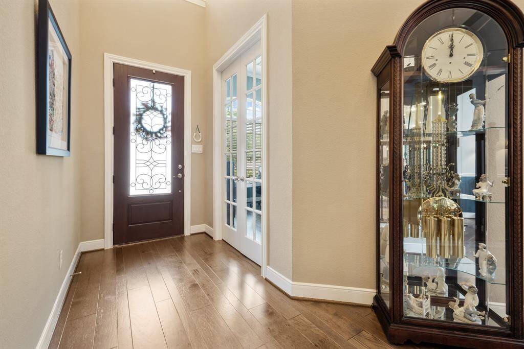 A welcoming entryway features a wooden and iron front door with decorative glass, leading to a bright space with engineered flooring. French doors offer a glimpse into the adjacent study.