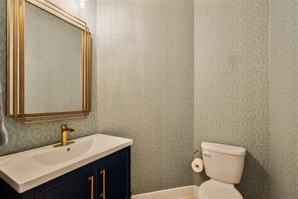 This bathroom features elegant Schumacher wallpaper, a modern vanity with a sleek white sink and gold faucet, and a matching gold-framed mirror.