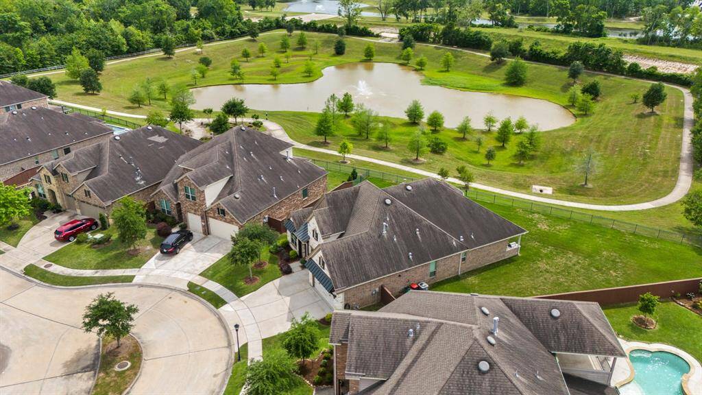 This photo showcases a beautiful suburban neighborhood with spacious homes featuring large driveways and well-maintained lawns. The area is lush with greenery and includes a scenic pond with a walking trail, providing a serene and picturesque setting.