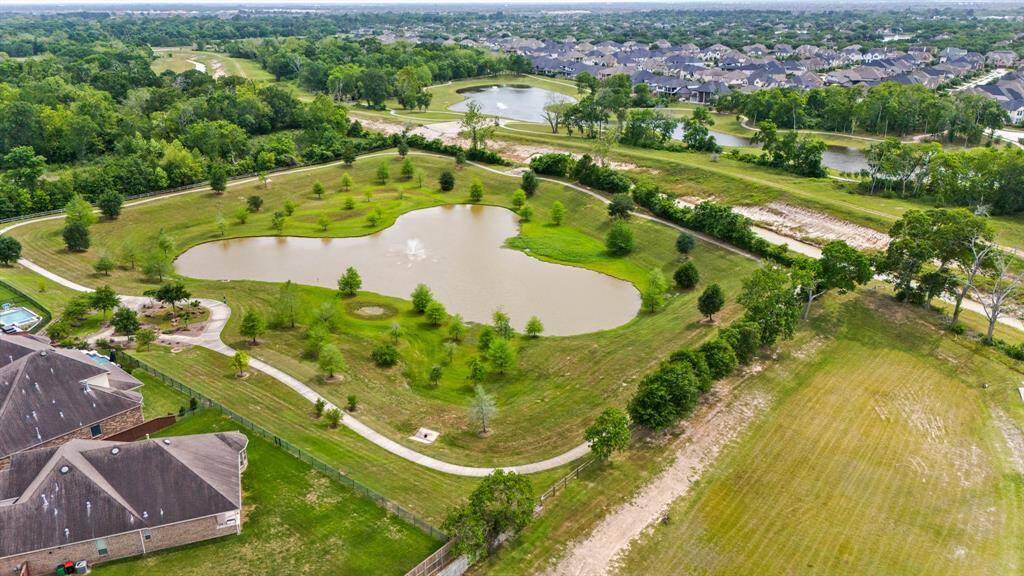 This photo showcases a serene residential area with a large pond and surrounding greenery. There are walking paths, nearby homes with spacious yards, and a peaceful neighborhood ambiance, ideal for nature lovers.