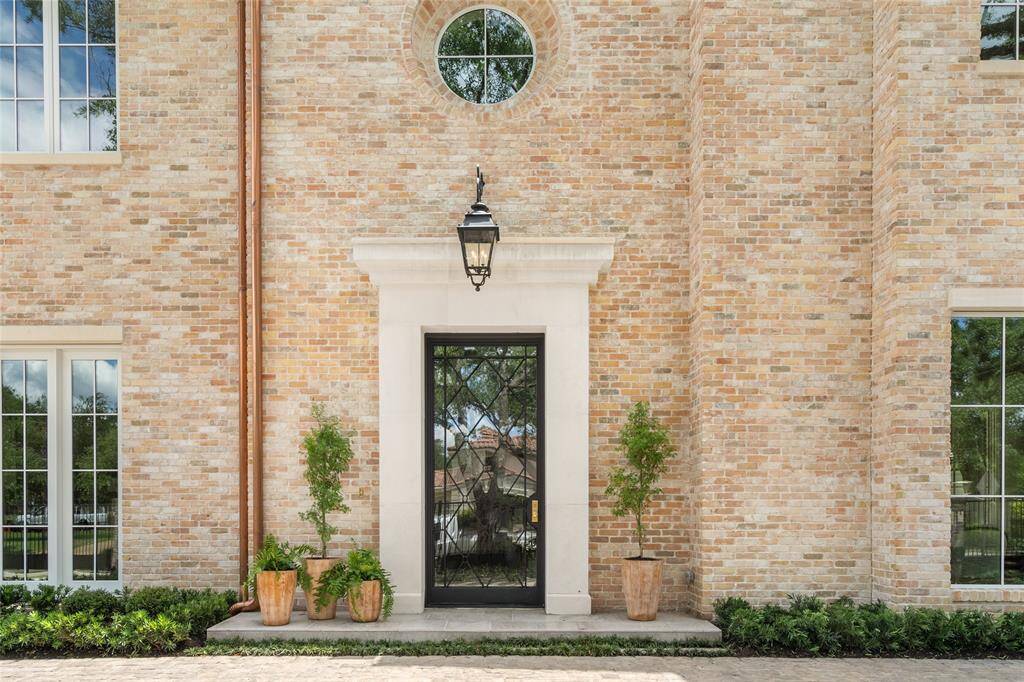 A handsome custom designed steel and glass front door with limestone surround, highlighted by an iron lantern, copper downspouts and accented by an elegant round window.