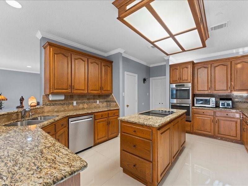The spacious kitchen features elegant wooden cabinetry, granite countertops, and modern stainless steel appliances, including a double oven and dishwasher.