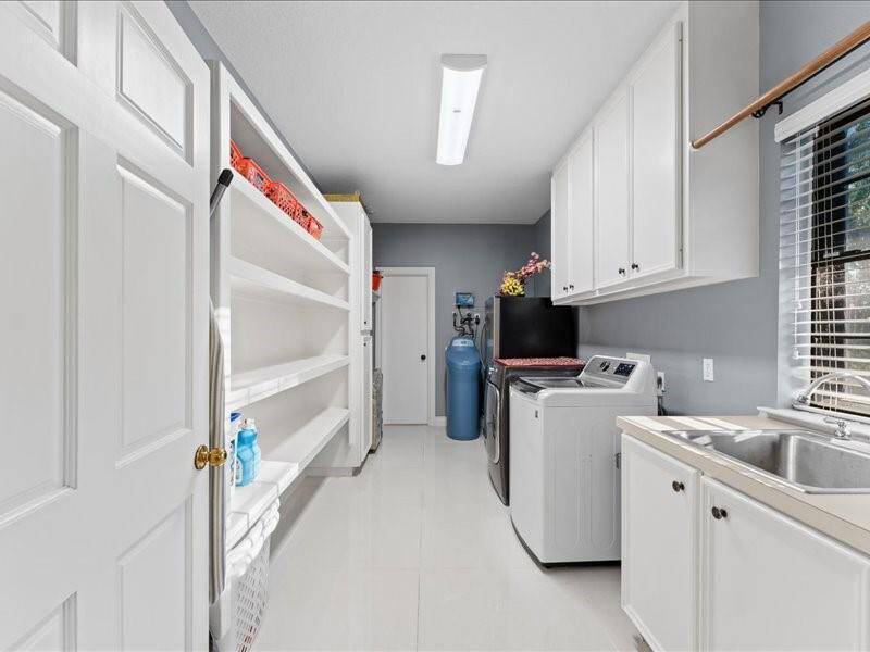 The modern, spacious laundry room features ample storage with built-in shelves and cabinets, a washer and dryer, and the utility sink.