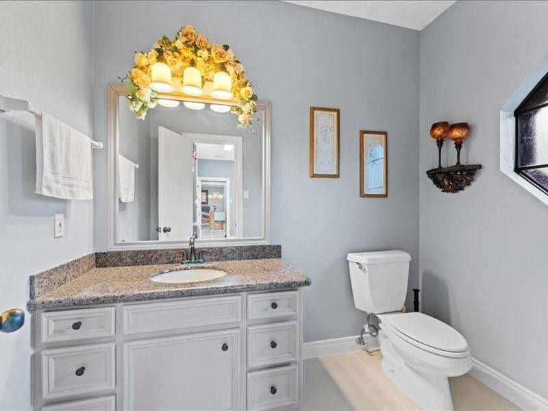 This half bathroom features a clean, elegant design with light blue walls, a granite countertop, and white cabinetry.