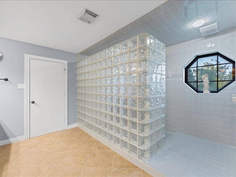 The master bathroom features a spacious walk-in shower with glass block walls and blue tiling offering a modern and bright feel.