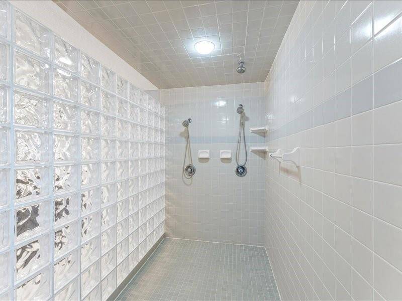 The master bathroom features a modern walk-in shower with dual shower heads, sleek glass block wall, and light gray tiling for a clean, contemporary look.