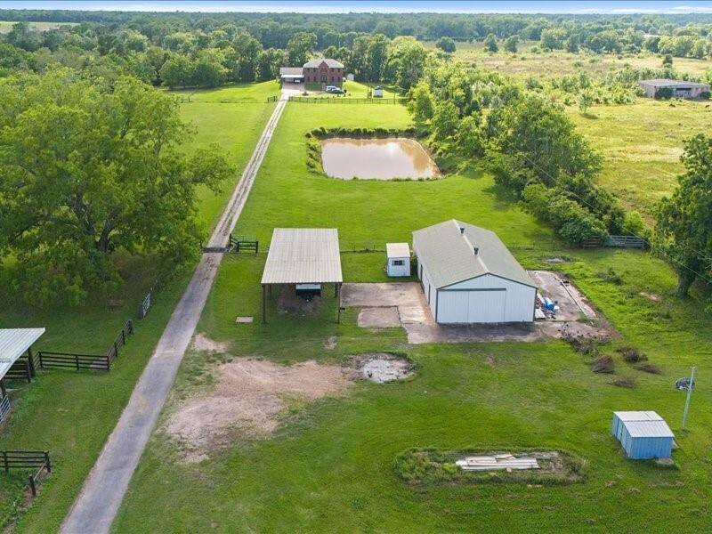 An aerial view of the country home featuring a long driveway leading to the house, a large barn, and a pond.