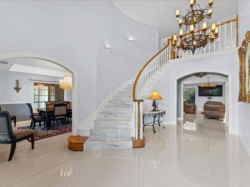 Stunning spiral staircase with marble like steps, a large chandelier, and glossy tile floors.