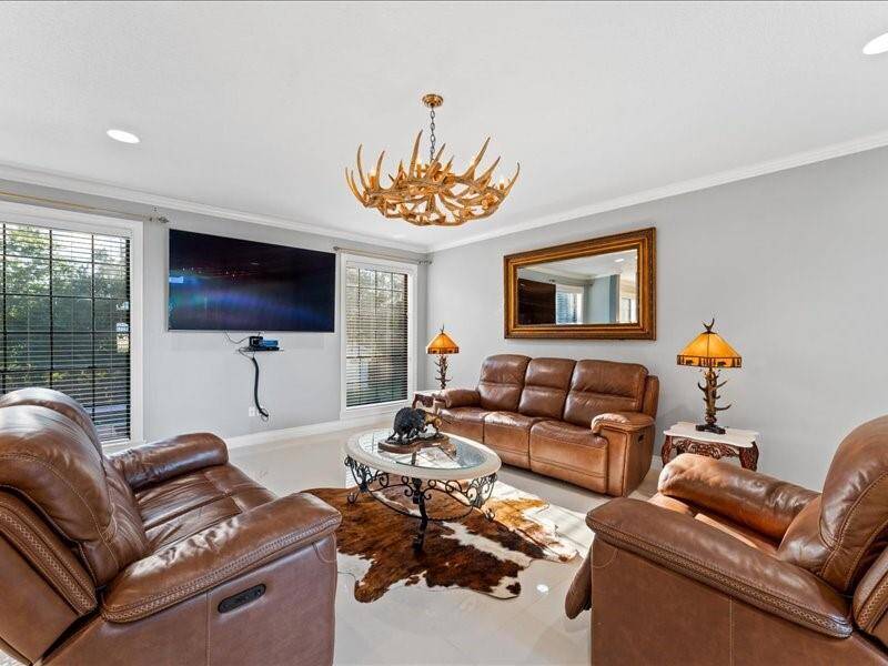 The cozy living room features a rustic antler chandelier, looking out the back porch and gunite pool, creating a warm and inviting atmosphere.