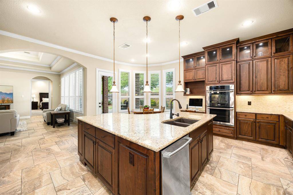 This stunning kitchen displays such a beautiful contrast with the dark stained cabinets, custom neutral paint, granite countertops, light modern backsplash, and SS appliances, oversized kitchen island with extra storage, breakfast bar, recessed lighting, high ceilings and walk in pantry.
