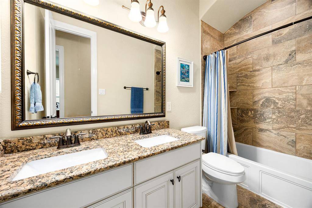 Secondary bath features tile flooring, bath/shower combo with tile surround, dark wood cabinets, beautiful light countertops, mirror, dark, sleek fixtures and modern finishes.