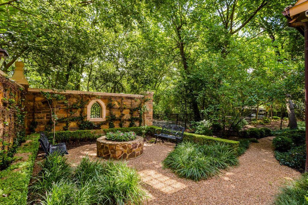 A side courtyard featuring privacy stone walls, lush landscaping, 2 benches and a lovely shaded pathway around the property.