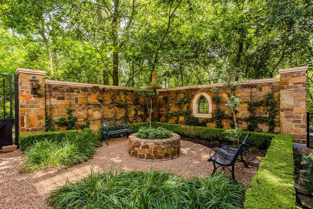 A side courtyard featuring privacy stone walls, lush landscaping, 2 benches and a lovely shaded pathway around the property.