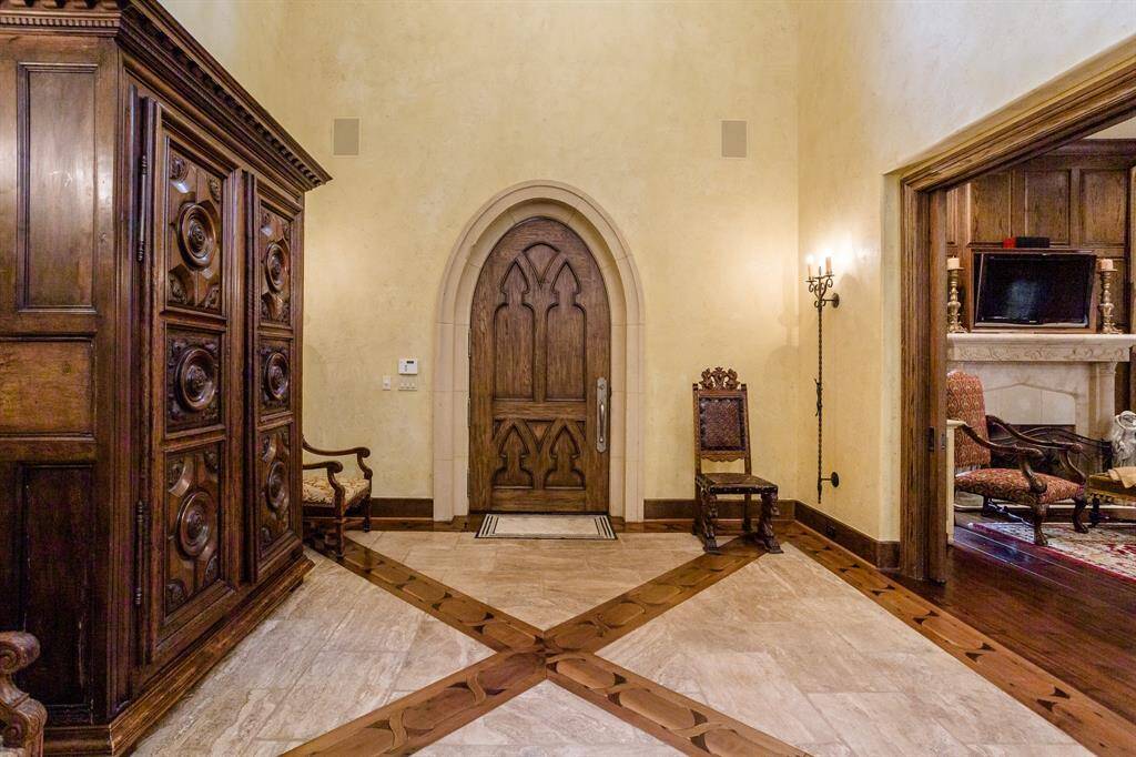 View of foyer and front door. Living room to the right. Pillowed travertine. Inlaid multiple-hardwood flooring. Ceiling 25'. Custom designed and built front door.