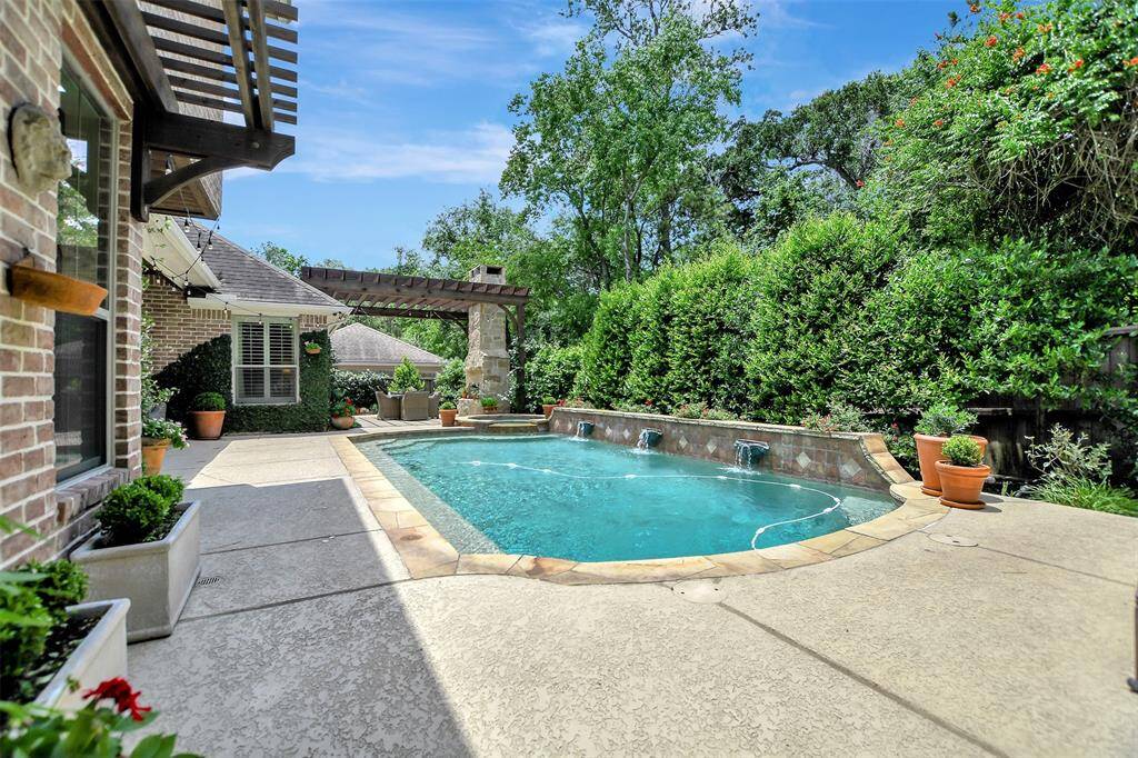 This inviting backyard features a sparkling pool with waterfall features, surrounded by lush greenery for privacy. A charming pergola, wood burning fireplace and cover patio area provide a perfect space for outdoor relaxation and entertaining.