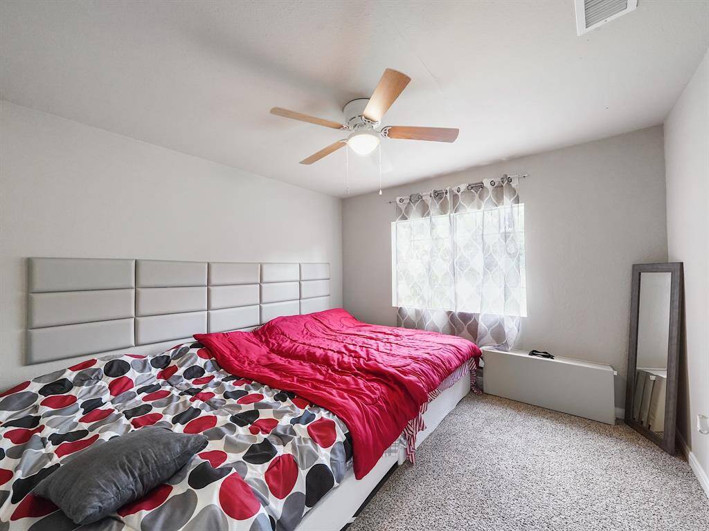 This spacious bedroom offers plush carpeting, a ceiling fan, and a large window overlooking the yard. The bed and soft finishes create a serene personal retreat.