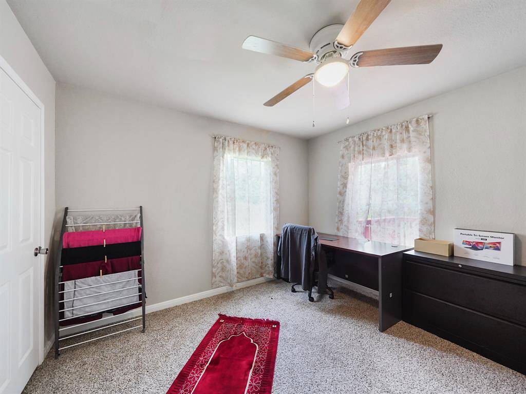 This carpeted room features generous natural light and a ceiling fan. It’s an excellent option for a dedicated workspace, already furnished with a large desk and matching storage.
