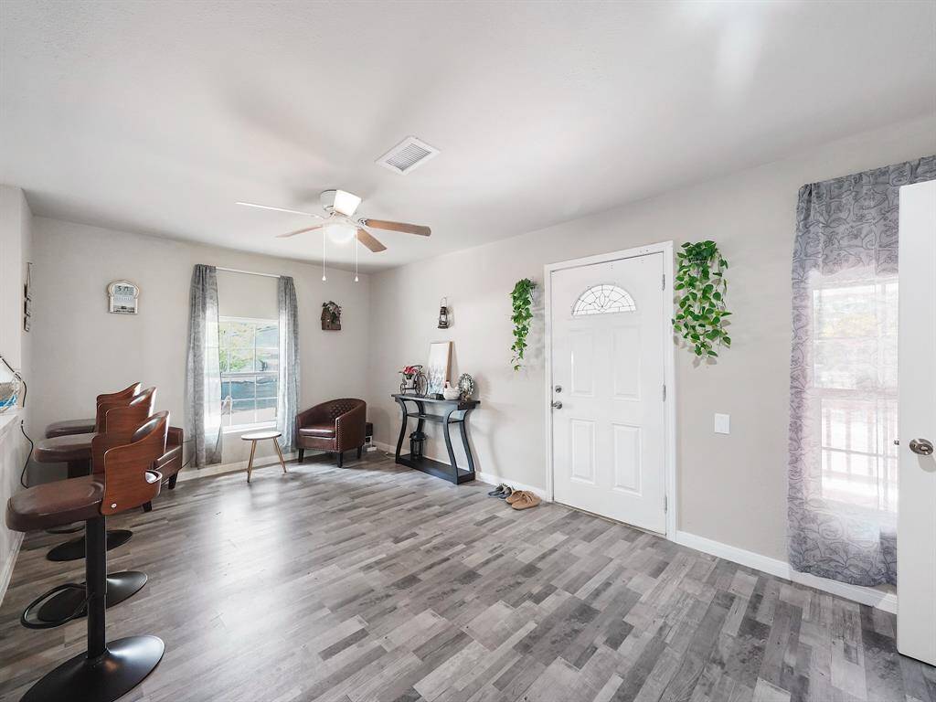 Behind the front door, you're greeted by a bright and furnished living space with large windows, ceiling fan, and durable vinyl flooring. Thoughtfully selected decor enhances the cozy ambiance.