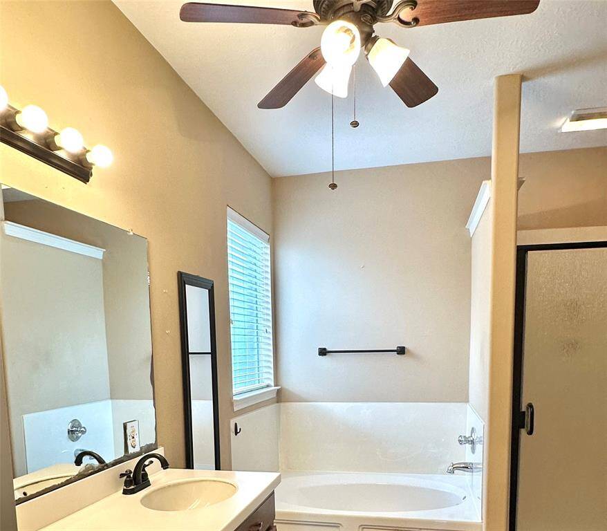 Primary bath includes double vanities, separate tub and shower, and ceiling fan
