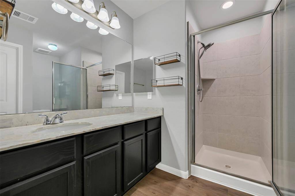 Primary bathroom with a quartz counter and so much storage. Notice the tiled walk-in shower with glass door.
