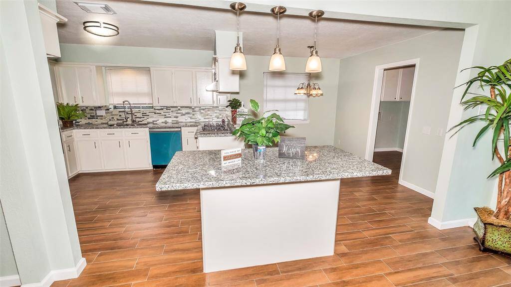 Large Granite Counter Island with Pendant lights in the middle next to Kitchen opens up to living room.